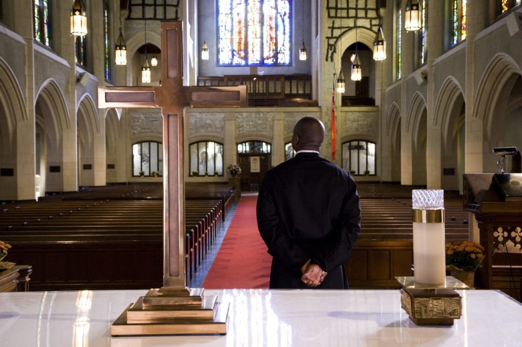 A father standing inside the church and behind him is a cross and a candle above the table